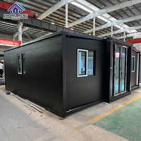 Casa Contenedor Expandible Negra Mate con Marcos de Ventana Blancos, Estructura de Acero Negro, Puerta de Vidrio, Diseño Prefabricado para Patio Trasero, Estudio o Villa