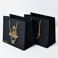 Sac d'emballage de vêtements haut de gamme personnalisé avec motif en relief doré et sac en papier à main noir.