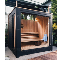 Sauna de exterior de gran tamaño con estructura de madera de hemlock, ventana de vidrio con marco negro, estufa Harvia, área de asientos en el alero y banco escalonado.