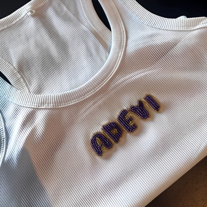 Camiseta sin mangas personalizada con bordado y aplique de nombre ADEYI con cuentas, blanca, con costuras cruzadas y bordados. - Product Image 1
