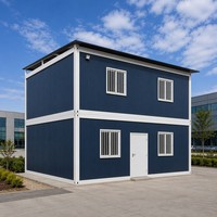 Maison conteneur démontable, revêtement bleu marine, structure blanche, deux étages avec balcon et escalier extérieur, pour usage bureautique ou en parc.