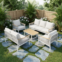 Ensemble de salon d'extérieur moderne en métal blanc, sièges à texture tressée, tables rondes avec accents en bois et coussins gris moelleux, idéal pour le patio