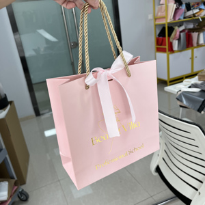 ถุงของขวัญกระดาษสีชมพูพิมพ์โลโก้ฟอยล์ทองแบบกำหนดเอง พร้อมโบว์ริบบิ้นผ้าซาติน ถุงกระดาษช้อปปิ้งสุดหรูสำหรับร้านเครื่องสำอางบูติก - Product Image 2