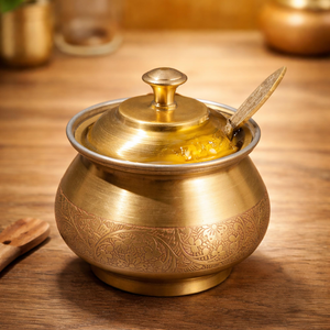 Timeless brass ghee <b>pot</b> accented by an intricate floral border engraving and a matching spoon. Available at wholesale price. - Product Image 1
