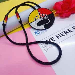 Collier artisanal avec pendentif patte d'ours perlé, sections jaunes, rouges, blanches et noires, et cordon long à suspendre sous la poitrine - Product Image 1