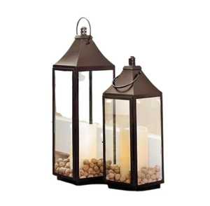 Paire de lanternes métalliques avec base carrée, panneaux de verre rectangulaires hauts, dessus pointu, poignée en boucle, bougies en forme de pilier, pierres décoratives - Product Image 1