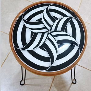 Mesa auxiliar redonda con un audaz patrón óptico en blanco y negro y patas minimalistas tipo horquilla, disponible a precios de mayorista. - Product Image 1