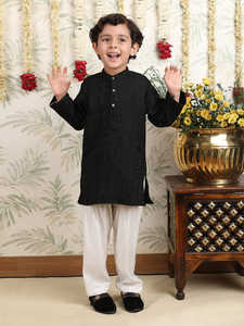 Niño con kurta negra y pijama, en pose de pie lateral, sonriendo, fondo festivo con decoración floral, atuendo tradicional elegante. - Product Image 3