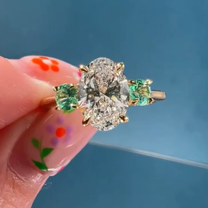 Bague à trois pierres en or 14 carats avec diamant ovale de 3,01 carats cultivé en laboratoire et pierres précieuses vertes rondes latérales, idéale pour fiançailles, promesse, fête ou comme cadeau. - Product Image 1