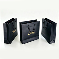 Sac cadeau en papier noir personnalisable de qualité supérieure avec impression de logo doré métallique et poignées en ruban plat pour l'emballage de produits de luxe