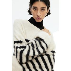 Belle femme modélisant un pull douillet et surdimensionné en fourrure avec des rayures noires audacieuses sur un col roulé noir. - Product Image 2