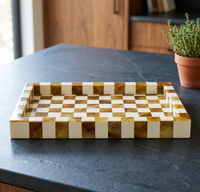 Bandeja rectangular a cuadros para servir con reloj y cadena dorados sobre mesa de madera