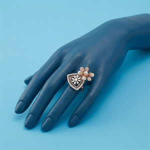 Une élégante bague en or rose ornée d'un motif floral avec des perles et des diamants, présentée sur un modèle de main stylisé bleu. - Product Image 1