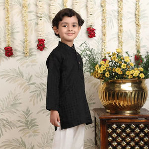 Niño con kurta negra y pijama, en pose de pie lateral, sonriendo, fondo festivo con decoración floral, atuendo tradicional elegante. - Product Image 1