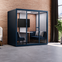 Pod lounge moderne bleu pour bureau, avec façade vitrée, sièges bleu marine, coussins gris clair et petite table