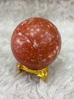 Bola kalsit oranye dengan warna amber yang cerah, kedalaman tembus pandang, bentuk halus, cahaya hangat, dan daya tarik mineral yang khas.