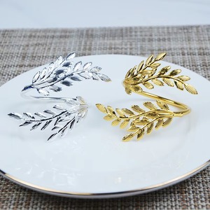 Anillos de servilleta de metal con diseño de hojas que añaden equilibrio visual a una mesa, anclando telas suaves con un elemento fuerte y pulido. - Product Image 4