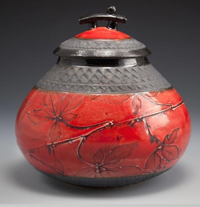 Urna funeraria roja profunda con motivos de hojas grabadas y una elegante tapa negra con un adorno decorativo. Disponible a precios de mayorista. - Product Image 3