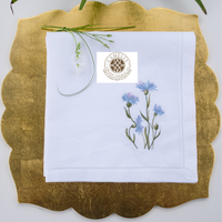 Lino natural con bordado de aciano, suave pero duradero, con vibrantes flores azules que añaden un toque fresco y elegante a las mesas.