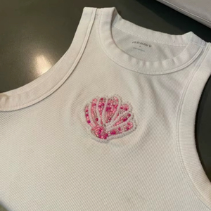 Top sin mangas de algodón acanalado blanco para mujer con bordado de alta calidad y parche de cuentas de vidrio de concha rosa, ideal para verano y playa. - Product Image 1