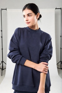 Joven mujer elegante en una sudadera extragrande de cuello redondo en color blanco puro, con un ajuste relajado y tela suave, posándose de manera informal en un estudio luminoso. - Product Image 2