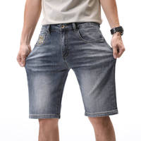 Shorts en jean bleu grisâtre délavé pour homme, style vintage, cinq poches, fermeture à boutons métalliques, logo brodé en jaune doré.