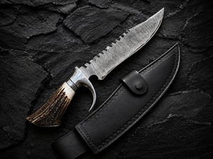 Cuchillo de caza hecho a mano de acero de Damasco con hoja fija de punta caída, filo dentado y mango de cuerno, con funda de cuero - Product Image 1