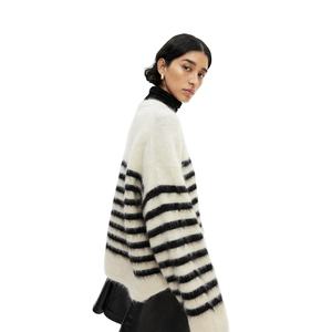 Belle femme modélisant un pull douillet et surdimensionné en fourrure avec des rayures noires audacieuses sur un col roulé noir. - Product Image 4