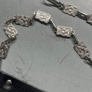 Ce produit est un accessoire vestimentaire des Highlands, décrit comme une chaîne sporran à motif celtique en nickel avec sangles en cuir noir. - Product Image 3