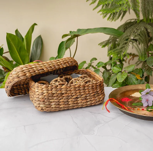 Small <b>rectangular</b> woven <b>basket</b> shown with its lid propped open on a table alongside festive ritual items available at wholesale. - Product Image 1
