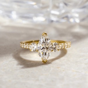 Anillo de compromiso con tres piedras de corte marquesa de 1.40 quilates, con piedras laterales redondas y banda pavé en oro amarillo de 14 quilates. - Product Image 1