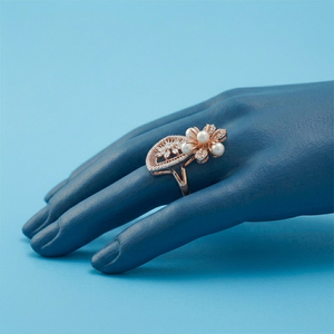 Une élégante bague en or rose ornée d'un motif floral avec des perles et des diamants, présentée sur un modèle de main stylisé bleu. - Product Image 2