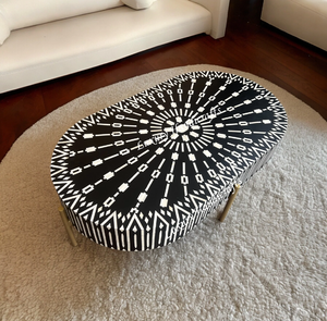 Mesa de centro ovalada con un diseño de incrustaciones geométricas y en forma de estrella en blanco y negro, sobre cuatro patas delgadas de latón. - Product Image 1