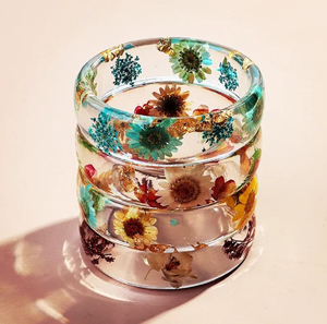 Impresionantes brazaletes apilados de resina transparente que exhiben margaritas secas de colores y brillantes copos de oro, disponibles a precios de mayorista. - Product Image 1