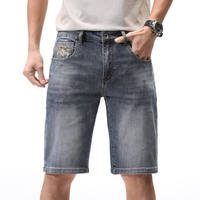 Shorts en jean bleu grisâtre délavé pour homme, style vintage, cinq poches, fermeture à boutons métalliques, logo brodé en jaune doré.