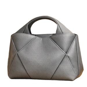 Esta elegante bolsa tote gris presenta un diseño geométrico acolchado con detalles en las esquinas plegadas y un cómodo asa superior. - Product Image 1