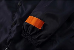 Veste coupe-vent noire pour homme avec accents de manches orange, ourlet rouge, cordon de serrage, boutons-pression, manches raglan et col rabattable - Product Image 3