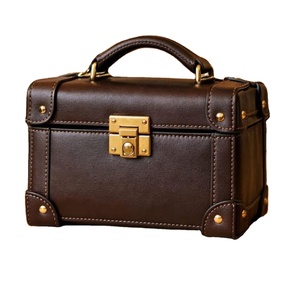 Este artículo es un bolso de mano con forma de baúl, hecho de cuero marrón, que recuerda a las maletas de viaje vintage. - Product Image 1
