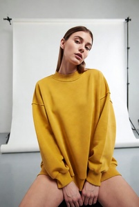 Joven mujer elegante en una sudadera extragrande de cuello redondo en color blanco puro, con un ajuste relajado y tela suave, posándose de manera informal en un estudio luminoso. - Product Image 5