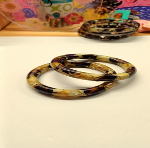 Pair of narrow resin bangles filled with golden leaf and brown <b>dried</b> botanical <b>petals</b>, available at wholesale prices. - Product Image 1