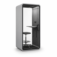 Cabine téléphonique de bureau moderne et compacte gris clair avec porte en verre arrondie, étagère de bureau et tabouret