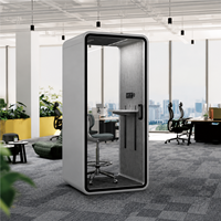 Cabine téléphonique de bureau moderne et compacte gris clair avec porte en verre arrondie, étagère de bureau et tabouret