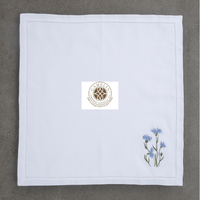 Lino natural con bordado de aciano, suave pero duradero, con vibrantes flores azules que añaden un toque fresco y elegante a las mesas.