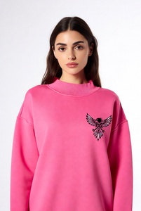 Hermosa mujer con una sudadera de cuello alto en un vibrante color rosa intenso, con delicado ribete de encaje y un audazco bordado de águila negra en el pecho. - Product Image 1