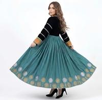 Femme portant une longue robe plissée bleu sarcelle avec un corsage en velours noir orné de bijoux tribaux en pièces d'argent et d'un motif soleil doré.