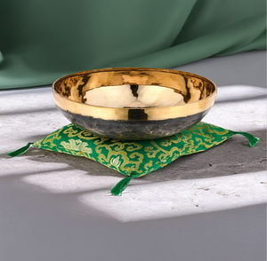 Cuenco tibetano de latón martillado con base oscura sobre una almohada verde bordada, disponible a precios de mayorista. - Product Image 1