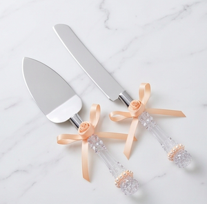 Elegante juego de cuchillo y espátula para pastel de bodas con mangos de cristal y detalles de cinta color melocotón para uso en fiestas. - Product Image 1